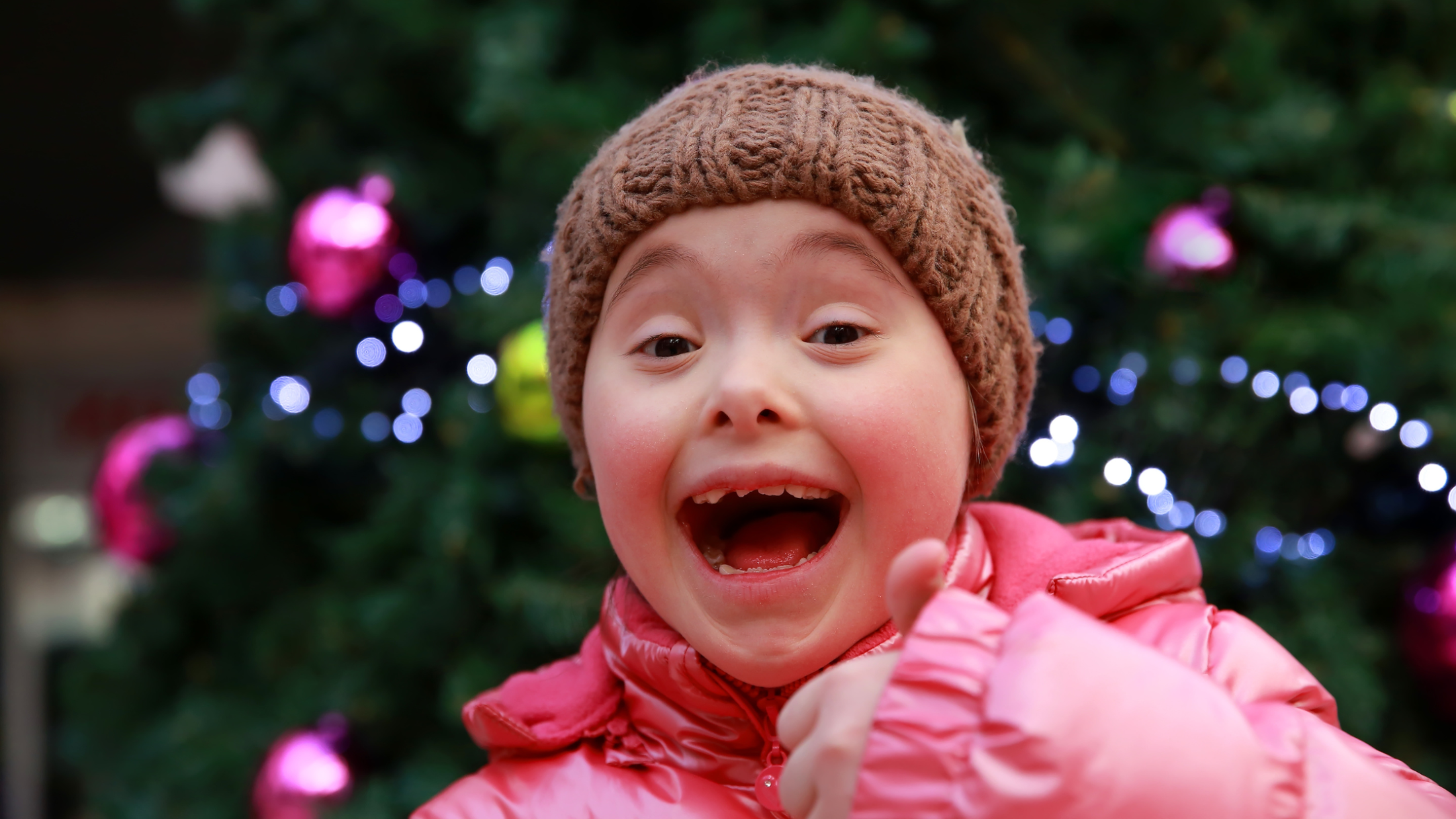 Child With A Big Smile And A Thumbs Up. Christmas Lights Glow Behind Them. 